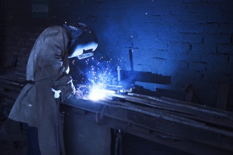 Man Wearing Welding Helmet Welding Metal Near Gray Brick Wall