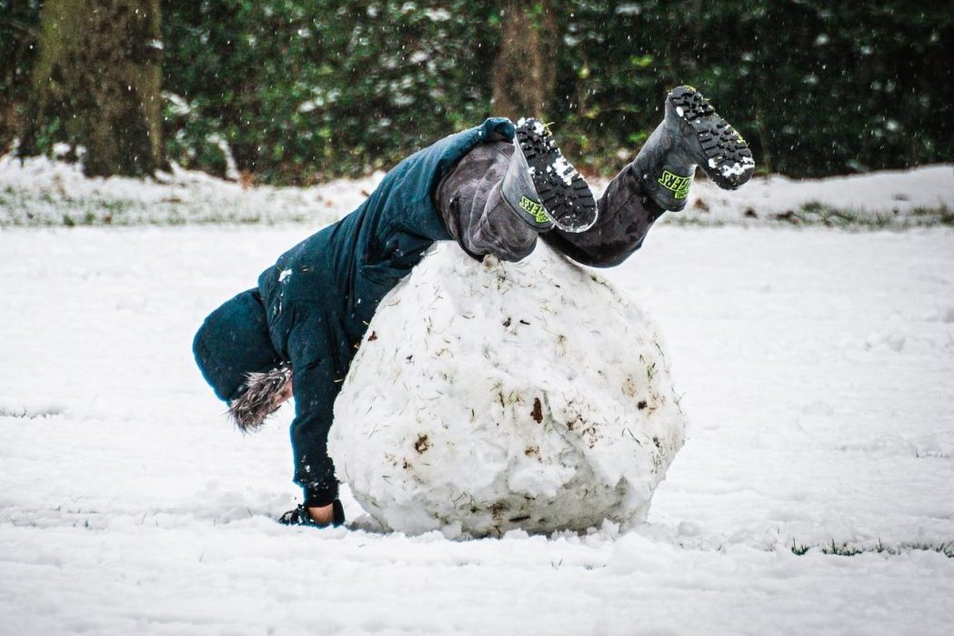 person in blue jacket and gray pants playing on snow covered ground during daytime